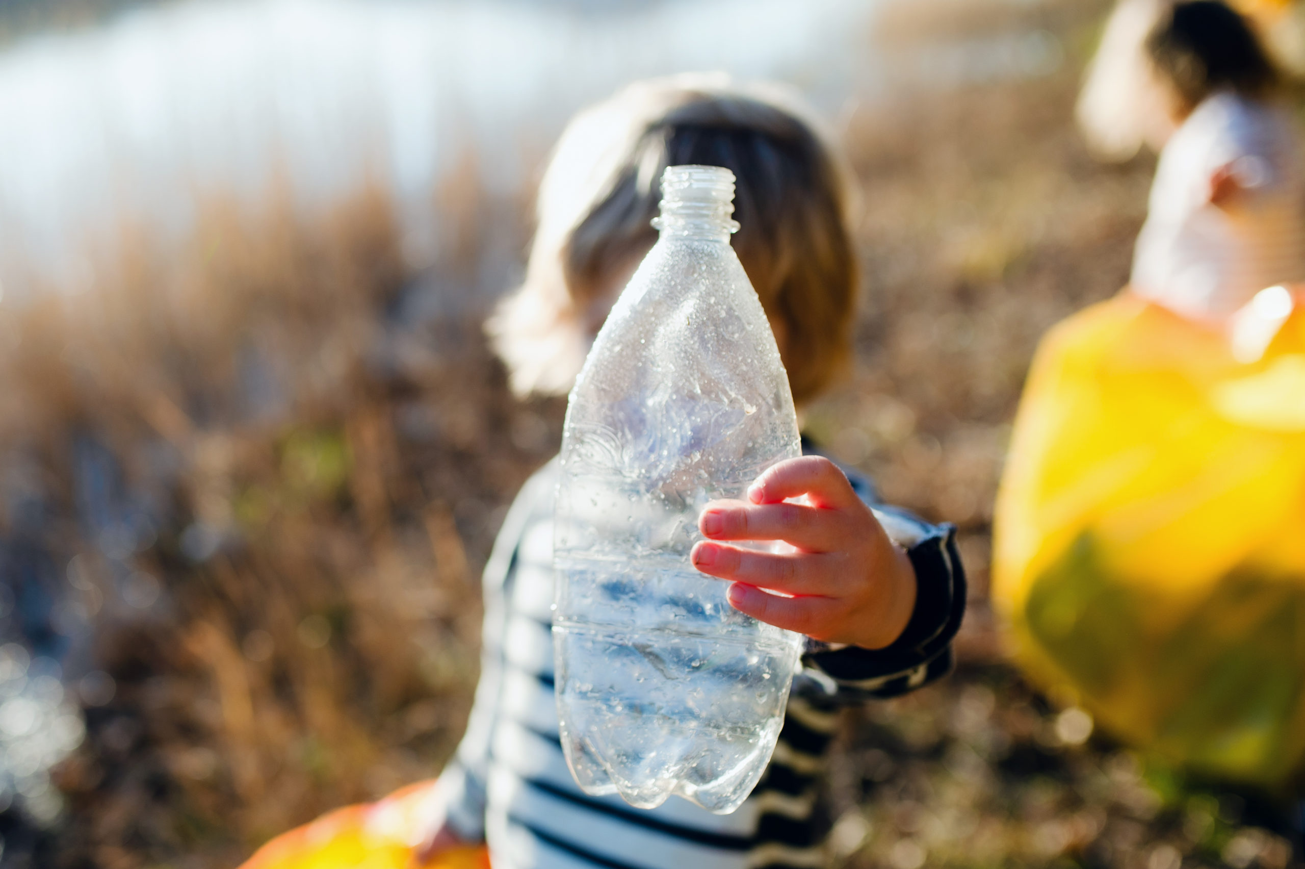 Un enfant tenant en main une bouteille en plastique érant dans la nature.
